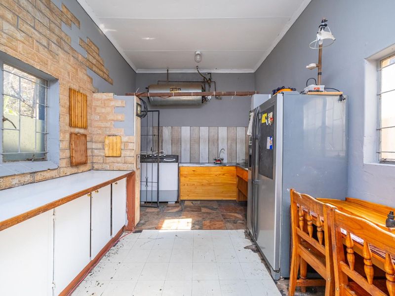 A functional kitchen space featuring exposed brickwork, built-in cabinetry, and a stainless steel sink, currently requiring cosmetic updates and maintenance.