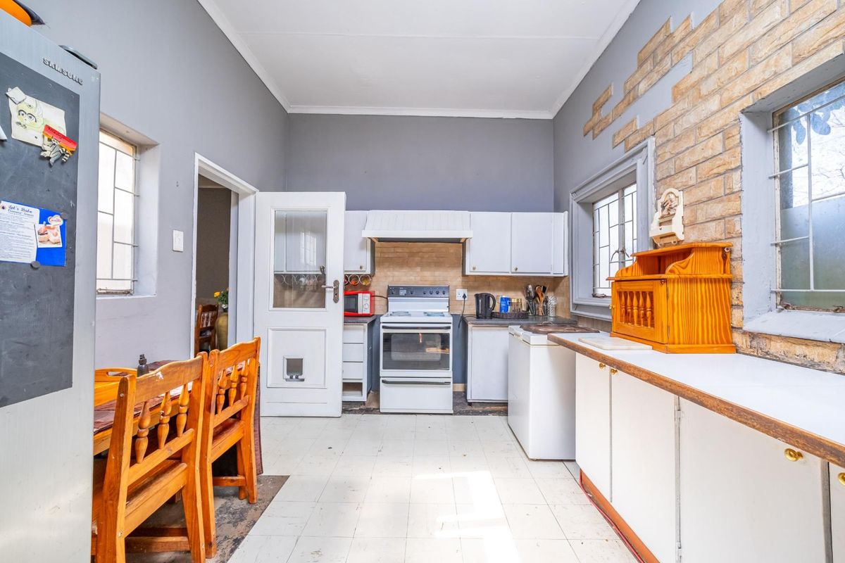 A functional kitchen featuring white cabinetry, a freestanding stove with extractor, and an exposed brick wall, offering potential for modernization and layout optimization.