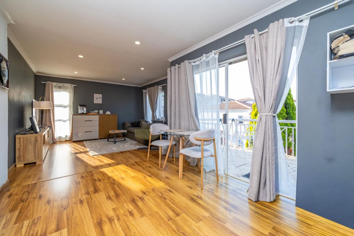 Bright and spacious living area featuring modern laminate flooring, recessed downlighting, and large sliding glass doors providing access to the balcony.