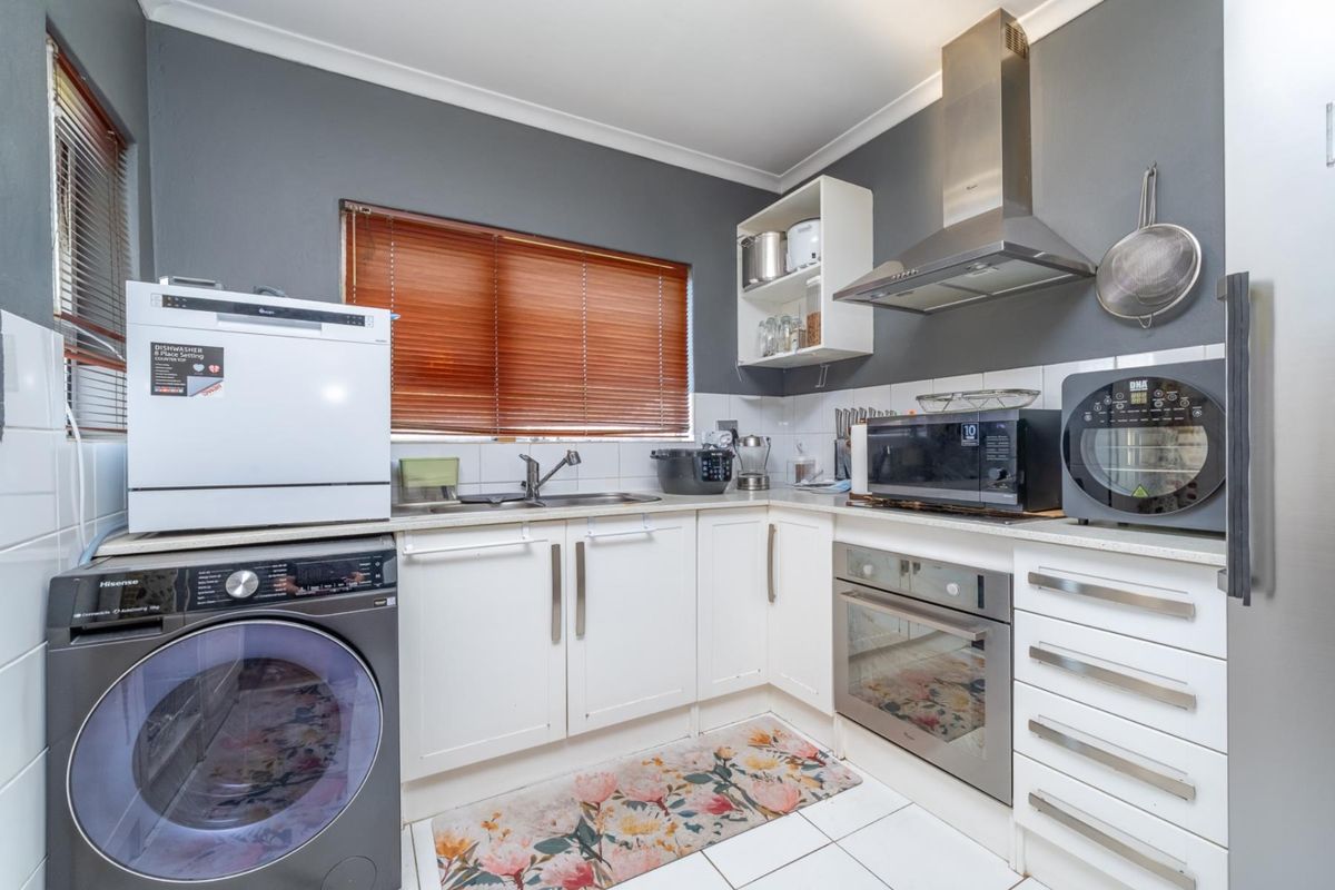 A functional kitchen featuring white cabinetry, stainless steel oven and extractor fan, tiled flooring, and a double sink with venetian blinds.