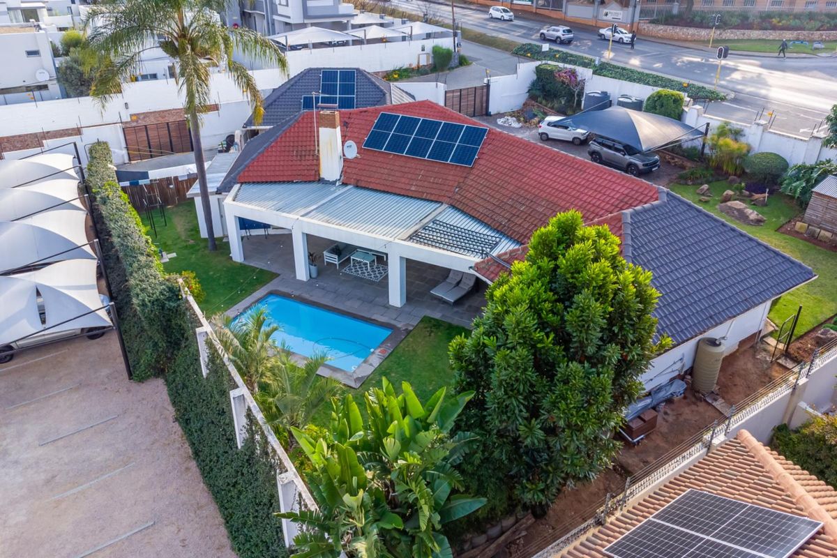 Aerial view of the property featuring a swimming pool, covered patio, solar panel installation, and secure perimeter walling with ample parking space.