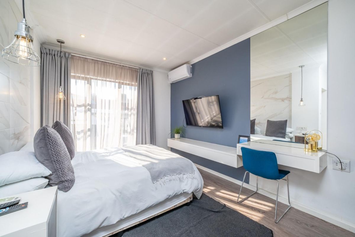 A well-appointed bedroom featuring a built-in floating vanity, large wall mirror, laminate flooring, and a wall-mounted air conditioning unit.