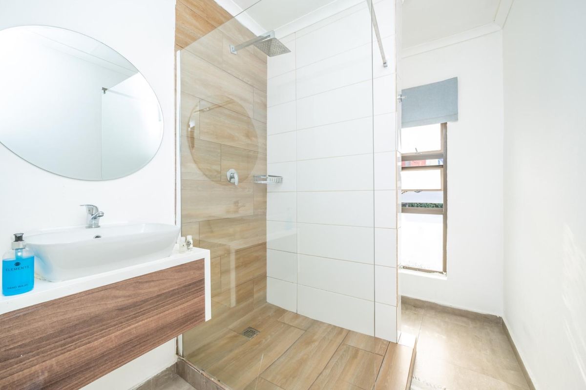 Modern bathroom featuring a floating vanity with vessel sink, a spacious walk-in shower with glass screen, and contemporary wood-look and white tiling.