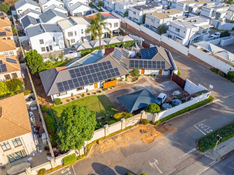 Aerial view of the guest house property featuring a large tiled roof with extensive solar panel installation, paved driveway, and landscaped garden area.