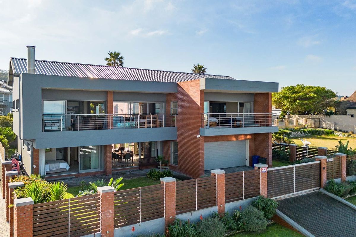 Aerial view of a modern two-story brick house featuring a spacious upper balcony, large sliding glass doors, and a secure fenced garden area.