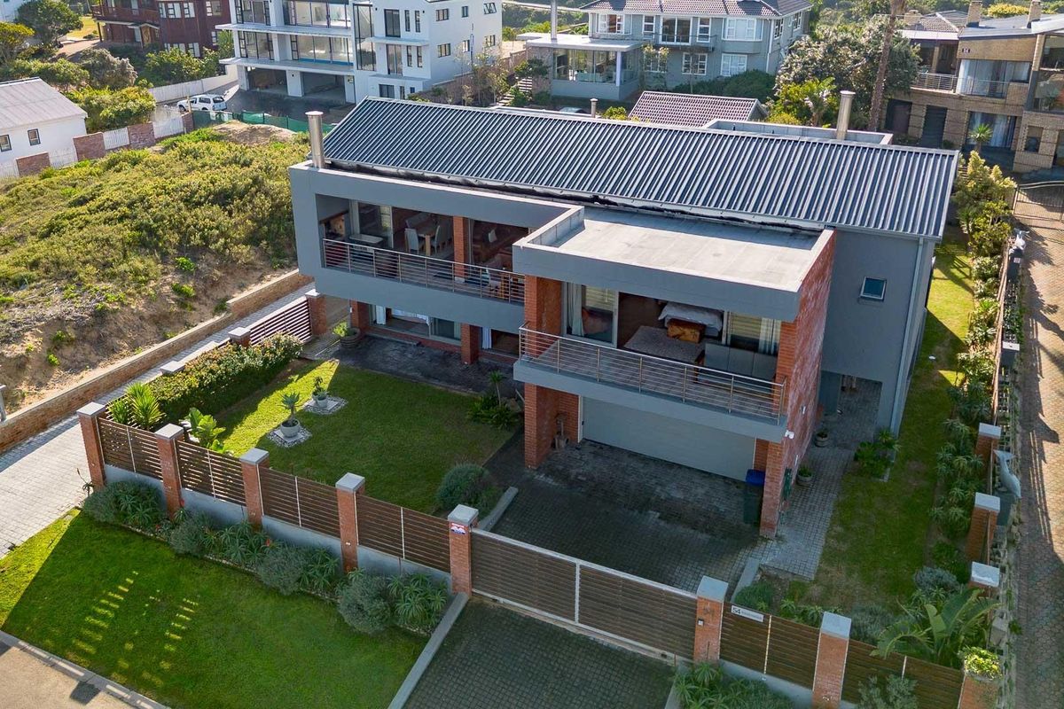 Aerial view of a modern two-story house featuring a corrugated metal roof, brick and grey facade, balconies, and a fenced garden area.
