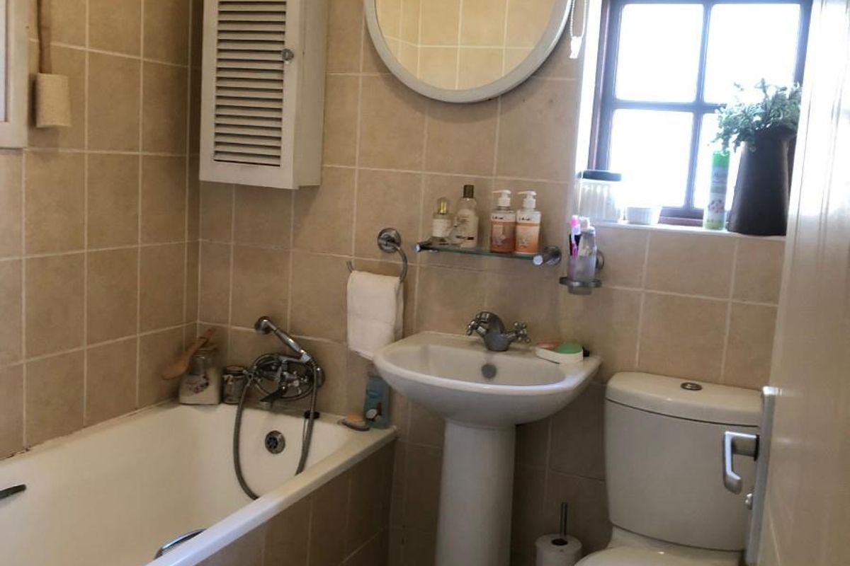 A functional bathroom featuring a pedestal basin, toilet, and bathtub with full-height wall tiling and a window for natural light.