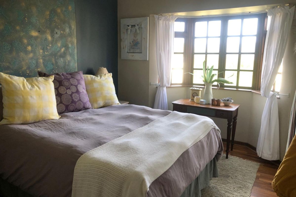 A cozy bedroom featuring a prominent bay window, timber flooring, and a dark accent wall, providing a comfortable and well-lit sleeping space.
