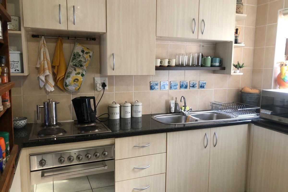 A functional kitchen featuring light wood-finish cabinetry, granite countertops, a built-in electric oven and hob, and a double sink with tiled backsplash.