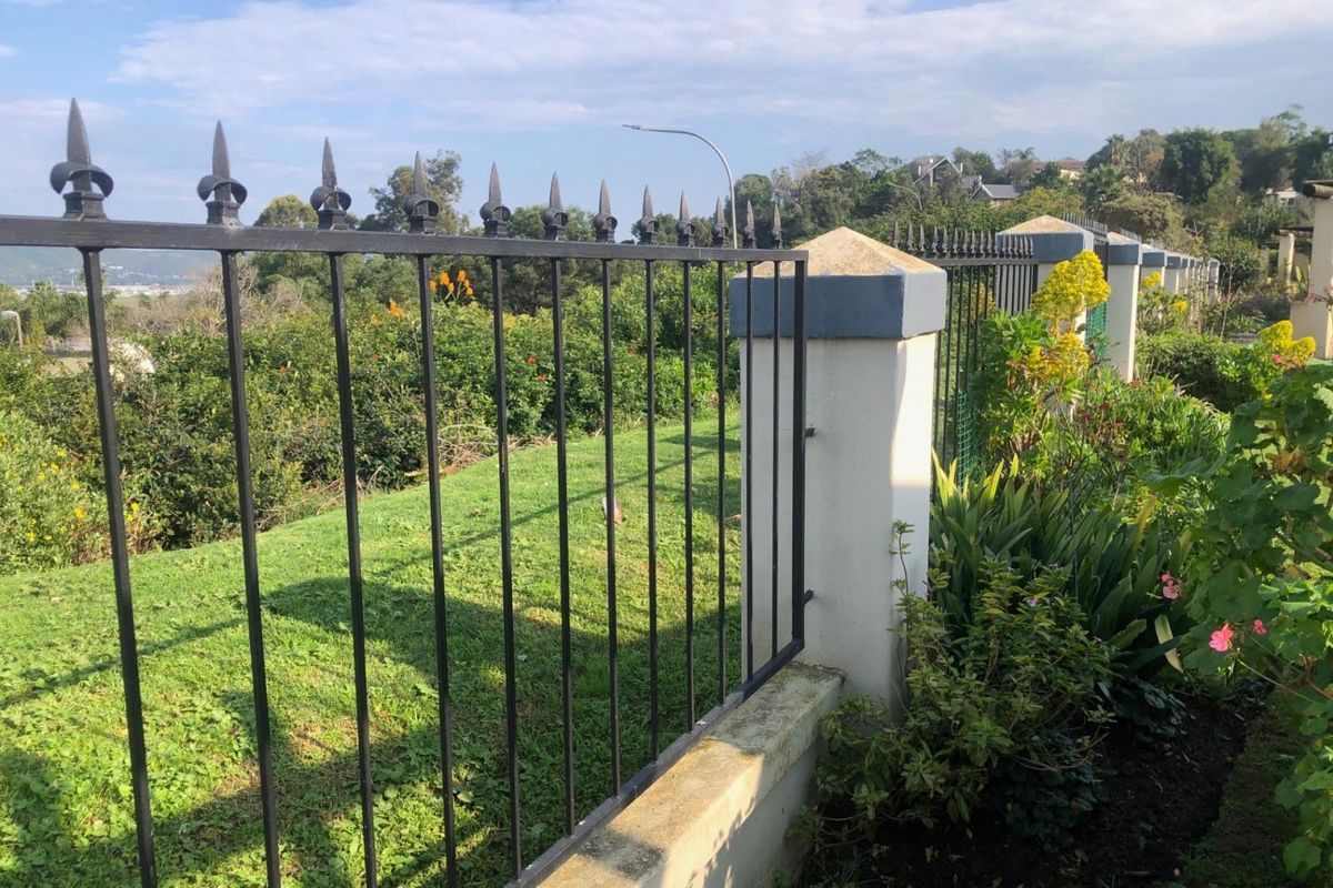 A secure boundary featuring a wrought iron fence mounted on masonry pillars, overlooking a landscaped garden area.