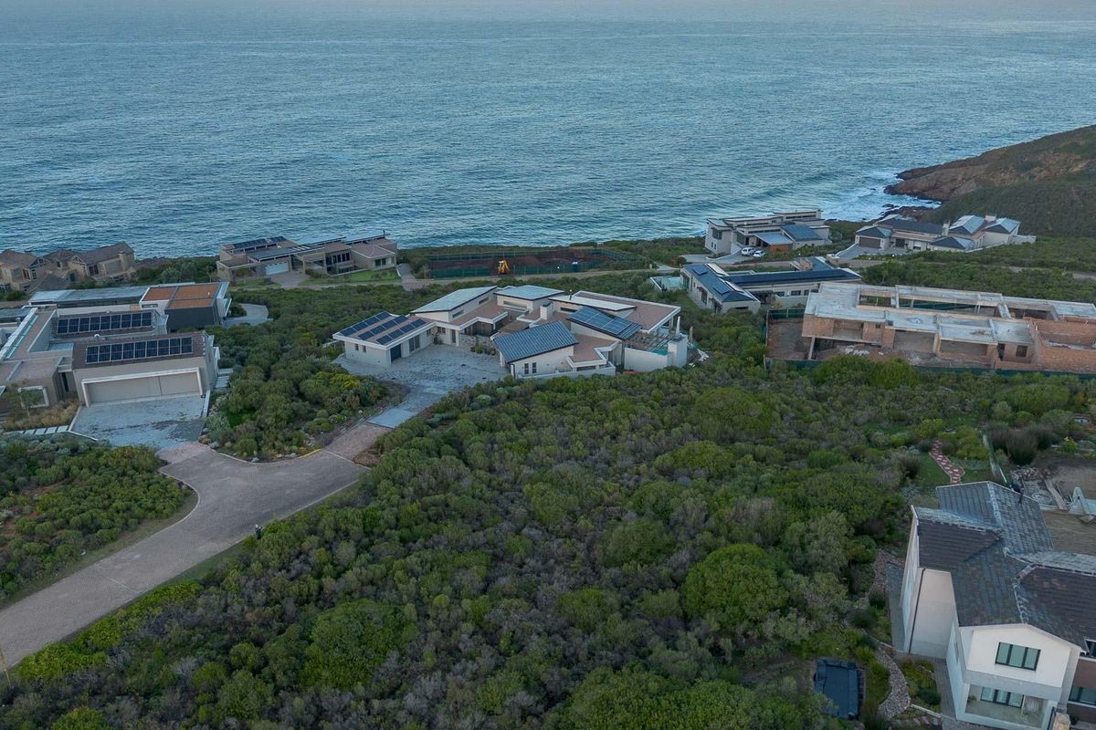 Aerial view of a coastal residential estate featuring multiple homes with solar installations, paved driveways, and direct ocean proximity.