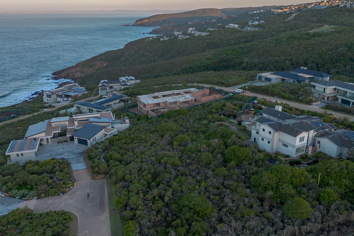 An aerial view of a coastal residential estate featuring established homes and a property under construction, set against a scenic ocean backdrop.