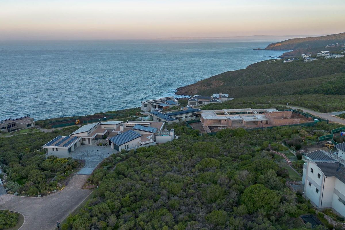 Aerial view of a coastal residential estate featuring modern homes, paved driveways, solar installations, and ongoing construction projects overlooking the ocean.