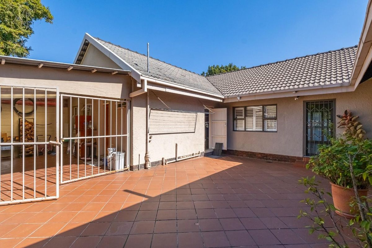 A spacious rear patio area featuring tiled flooring, security gates, and direct access to the main dwelling, suitable for outdoor entertaining.