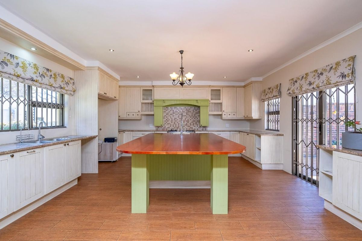 Spacious kitchen featuring a large central island, ample built-in cabinetry, double sink, and tiled flooring with direct access to the outdoor area.