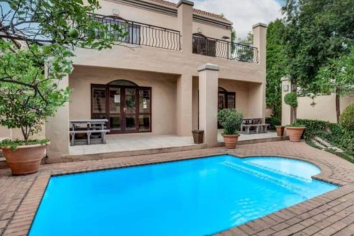Rear view of the apartment featuring a swimming pool, paved patio area, and an upper-level balcony with wrought iron railings.