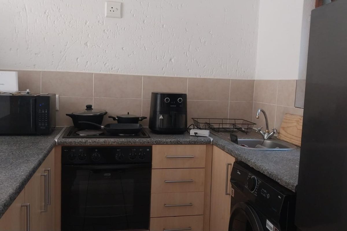 Compact kitchen featuring laminate cabinetry, granite countertops, built-in oven, hob, and a stainless steel sink with tiled splashback.