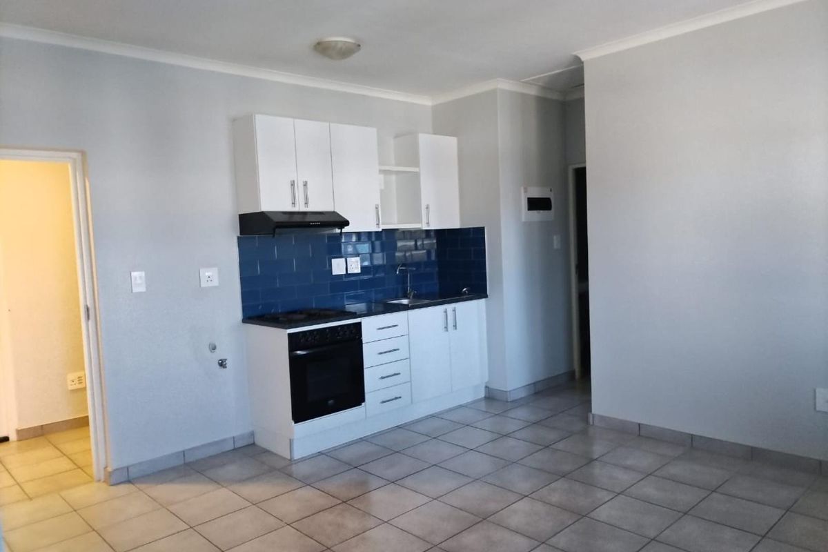 Compact kitchen featuring white cabinetry, a dark countertop, blue tiled backsplash, and built-in oven with extractor fan, set against neutral tiled flooring.