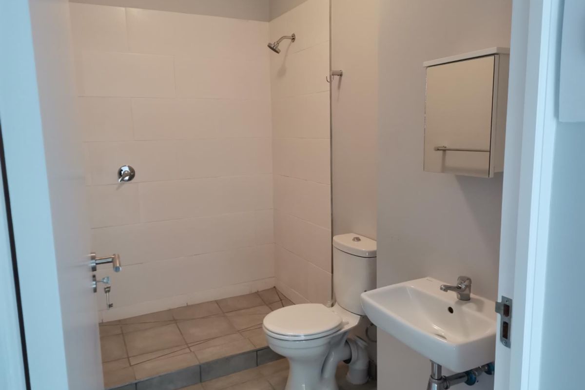 A clean, functional bathroom featuring a walk-in shower, wall-mounted basin, toilet, and a wall-mounted medicine cabinet with neutral tiling.