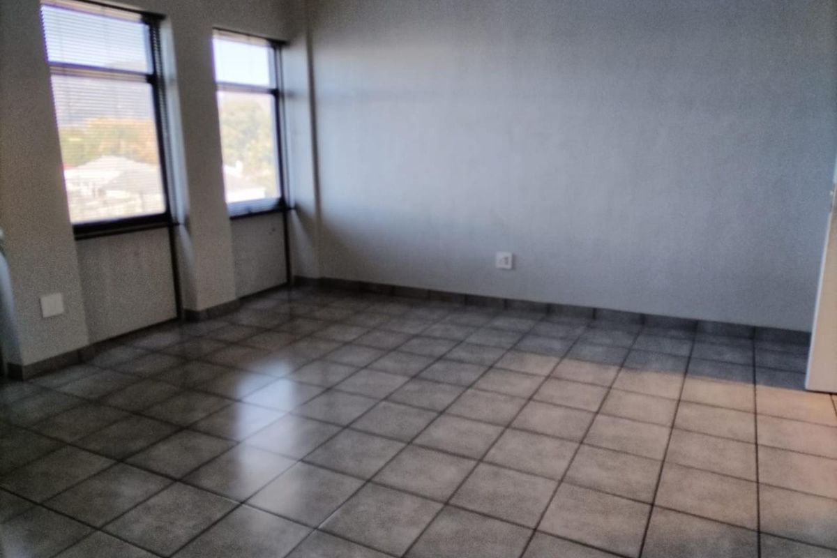 An empty, neutrally painted living area featuring tiled flooring and large windows with fitted venetian blinds, offering a blank canvas for interior design.