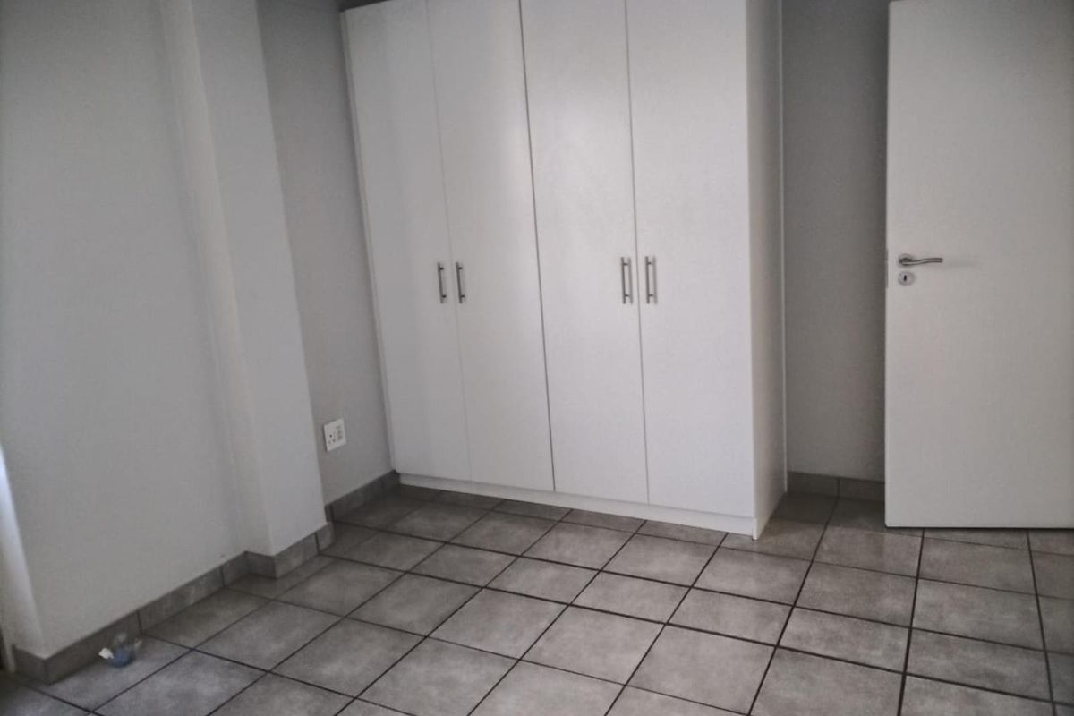 A clean, empty bedroom featuring neutral tiled flooring and white built-in cupboards, providing a versatile space ready for personalization.