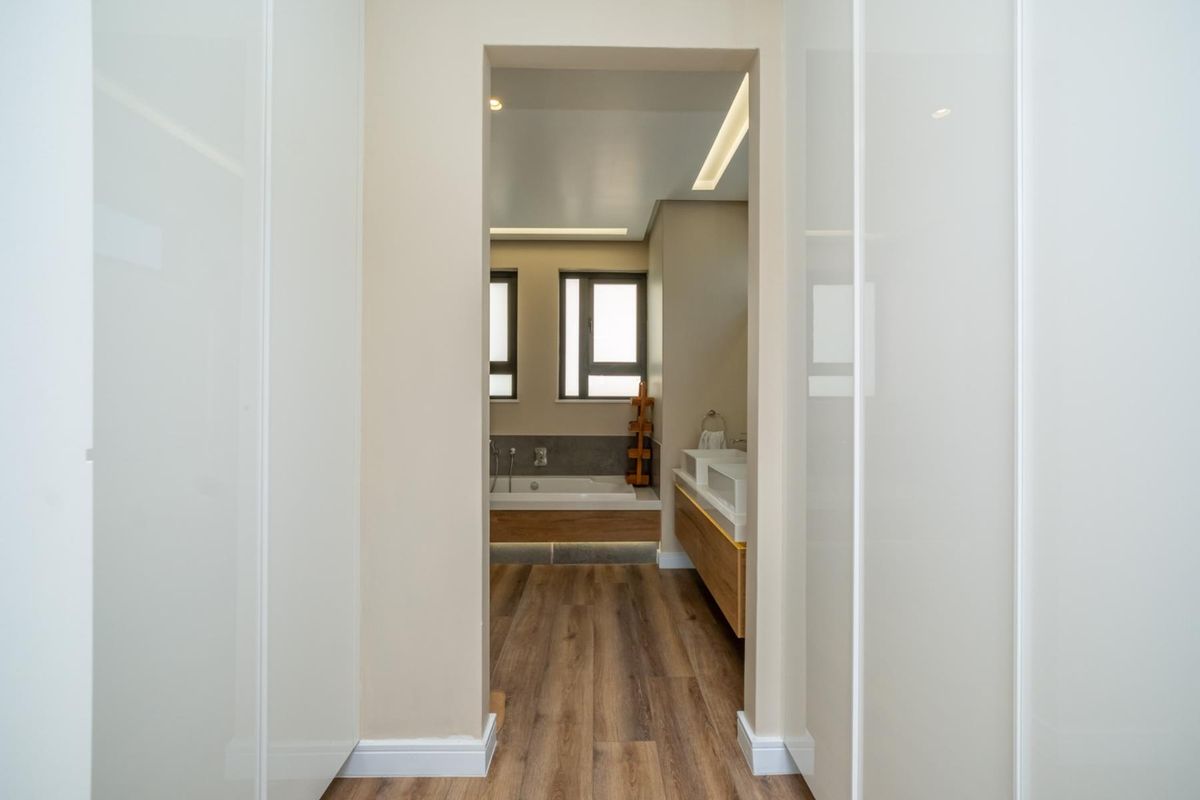 A modern bathroom featuring a built-in vanity, bathtub, and sleek cabinetry, viewed through a hallway with integrated storage.