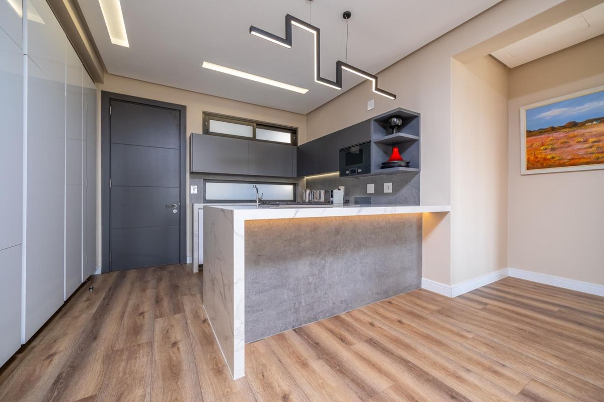 Modern kitchen featuring sleek grey cabinetry, a stone-topped island with integrated lighting, and high-quality laminate flooring in a contemporary apartment setting.