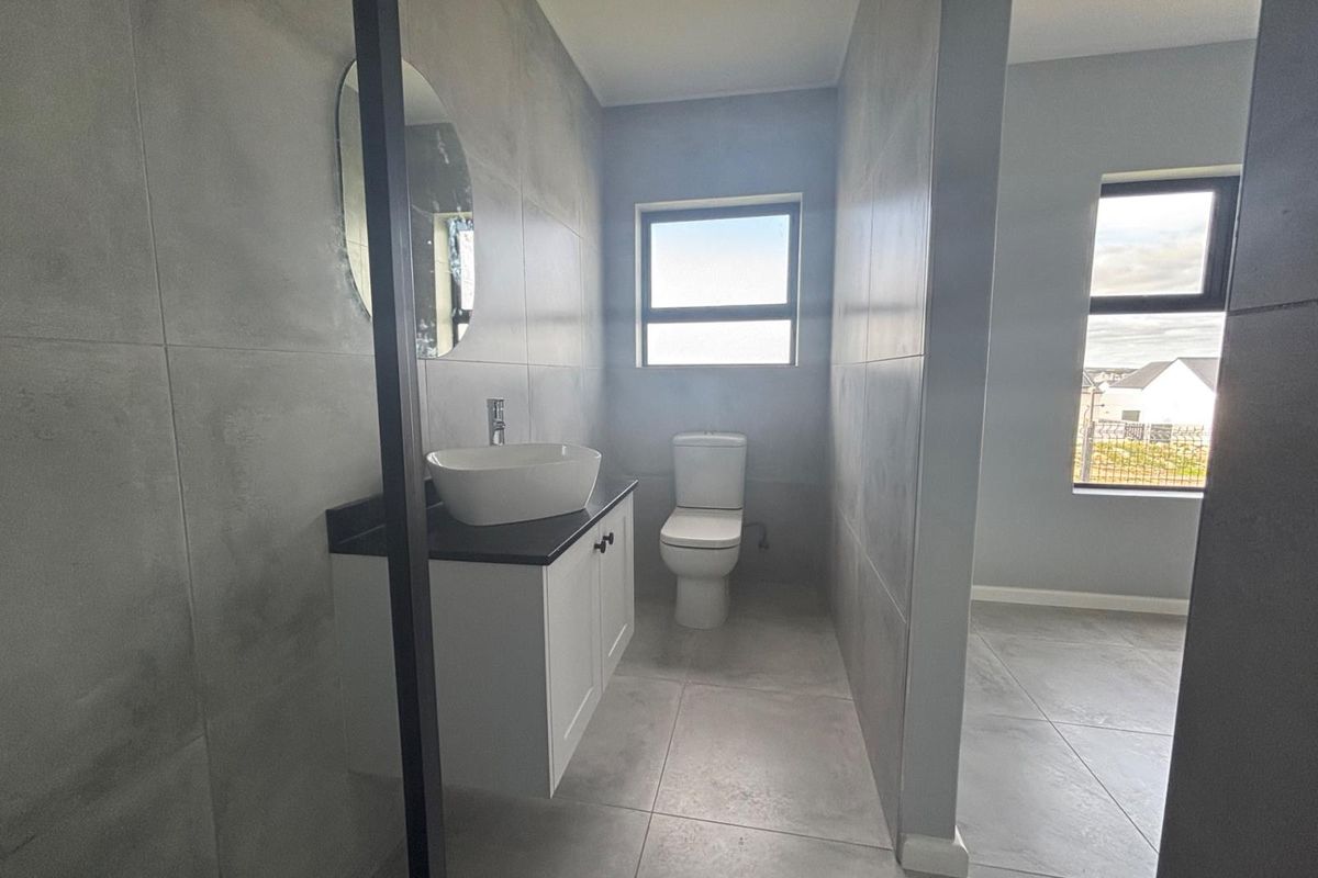 Modern bathroom featuring large format grey tiling, a wall-mounted vanity with a vessel sink, and a clean, minimalist aesthetic.