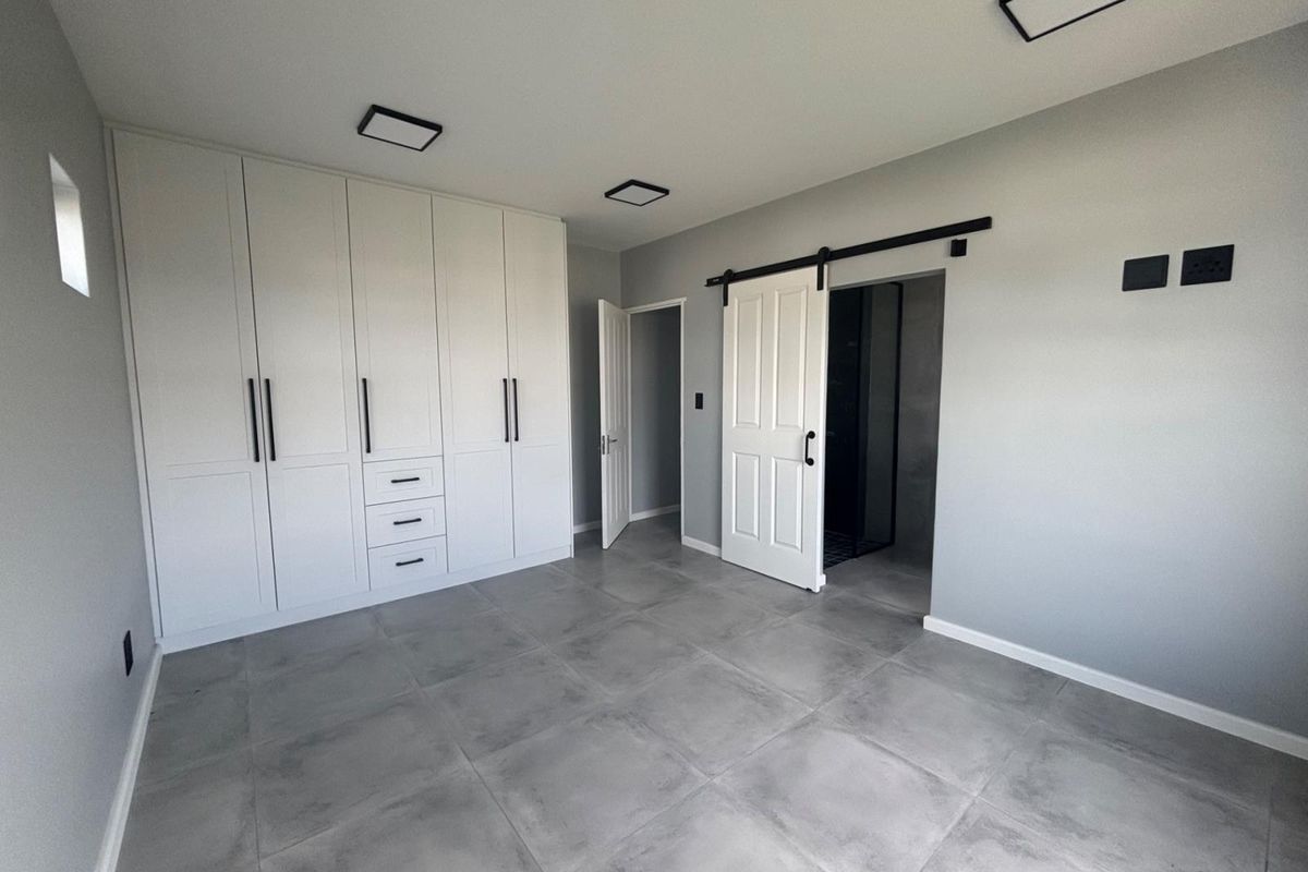 A modern, empty bedroom featuring neutral grey tiled floors, extensive built-in cabinetry, and a stylish sliding barn door leading to an en-suite bathroom.