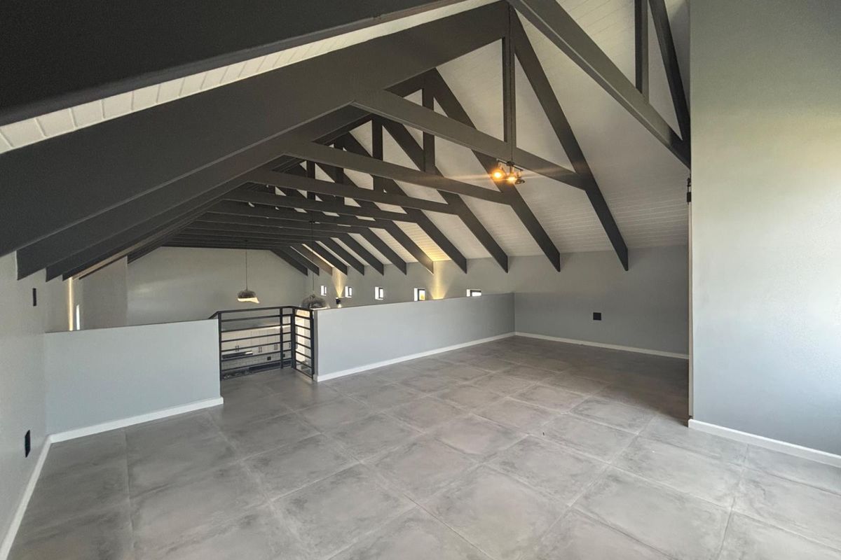 Spacious mezzanine living area featuring high vaulted ceilings with exposed dark timber trusses and modern grey floor tiles.