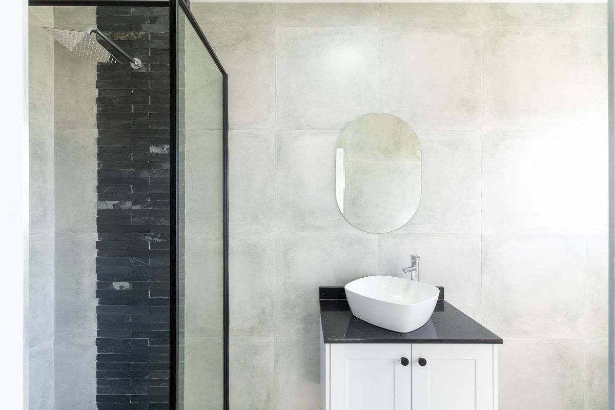 Modern bathroom featuring a sleek vanity with vessel sink, stone countertop, and a walk-in shower with a rain shower head and feature tiling.