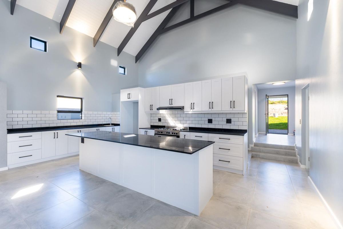 Modern, spacious kitchen featuring a large central island, granite countertops, subway tile backsplash, and high vaulted ceilings with exposed rafters.