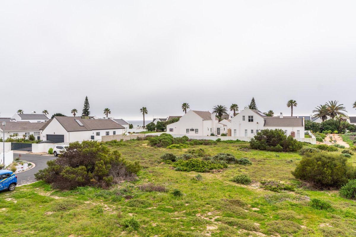 An aerial view of a residential neighborhood featuring white houses with tiled roofs, paved driveways, and surrounding coastal vegetation.
