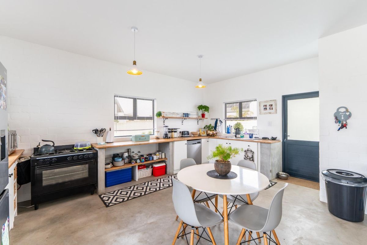 A bright, industrial-style kitchen featuring concrete countertops, open base cabinetry, a gas stove, and polished concrete flooring with direct exterior access.