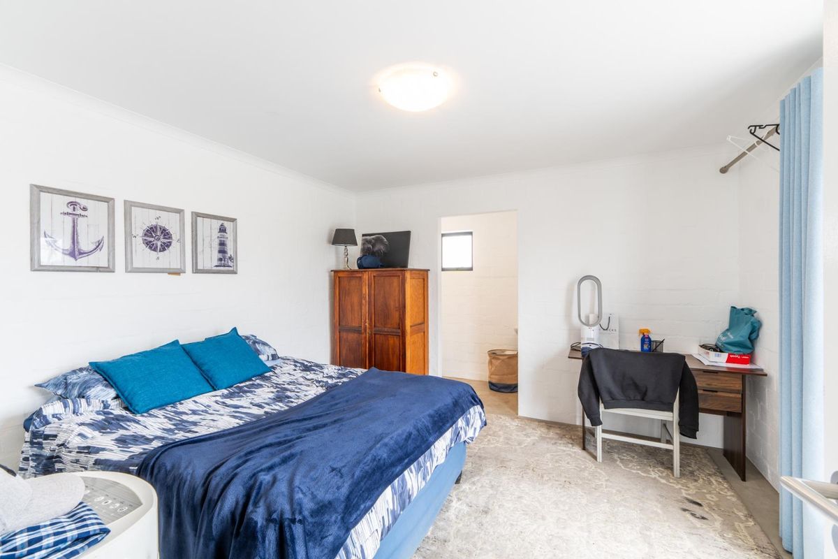 A bedroom featuring painted brick walls, coving, and a central ceiling light fixture, with an adjoining space visible through the doorway.
