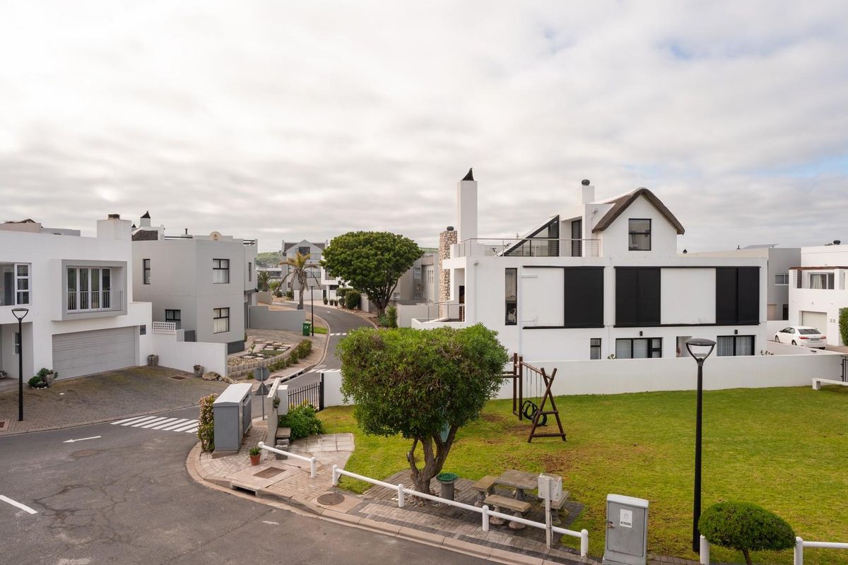 An elevated aerial view of a modern residential estate featuring contemporary white homes, paved streets, and landscaped communal green spaces.