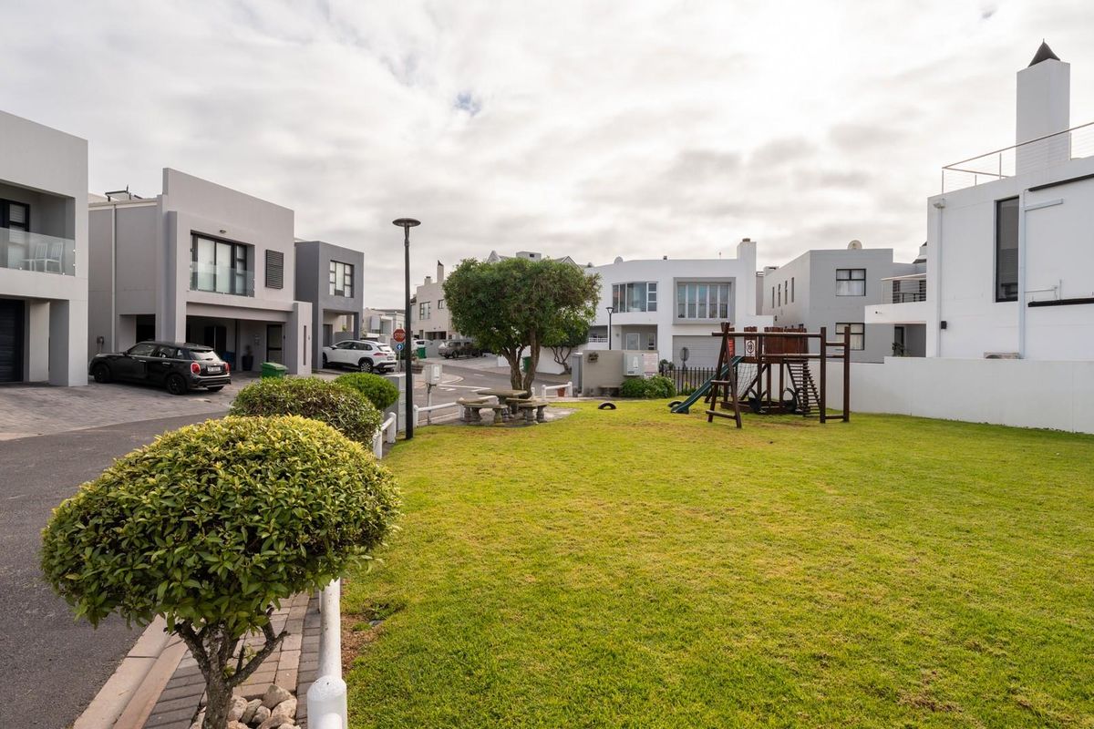 A view of the residential complex featuring a well-maintained communal lawn area, paved driveways, and modern architectural facades.