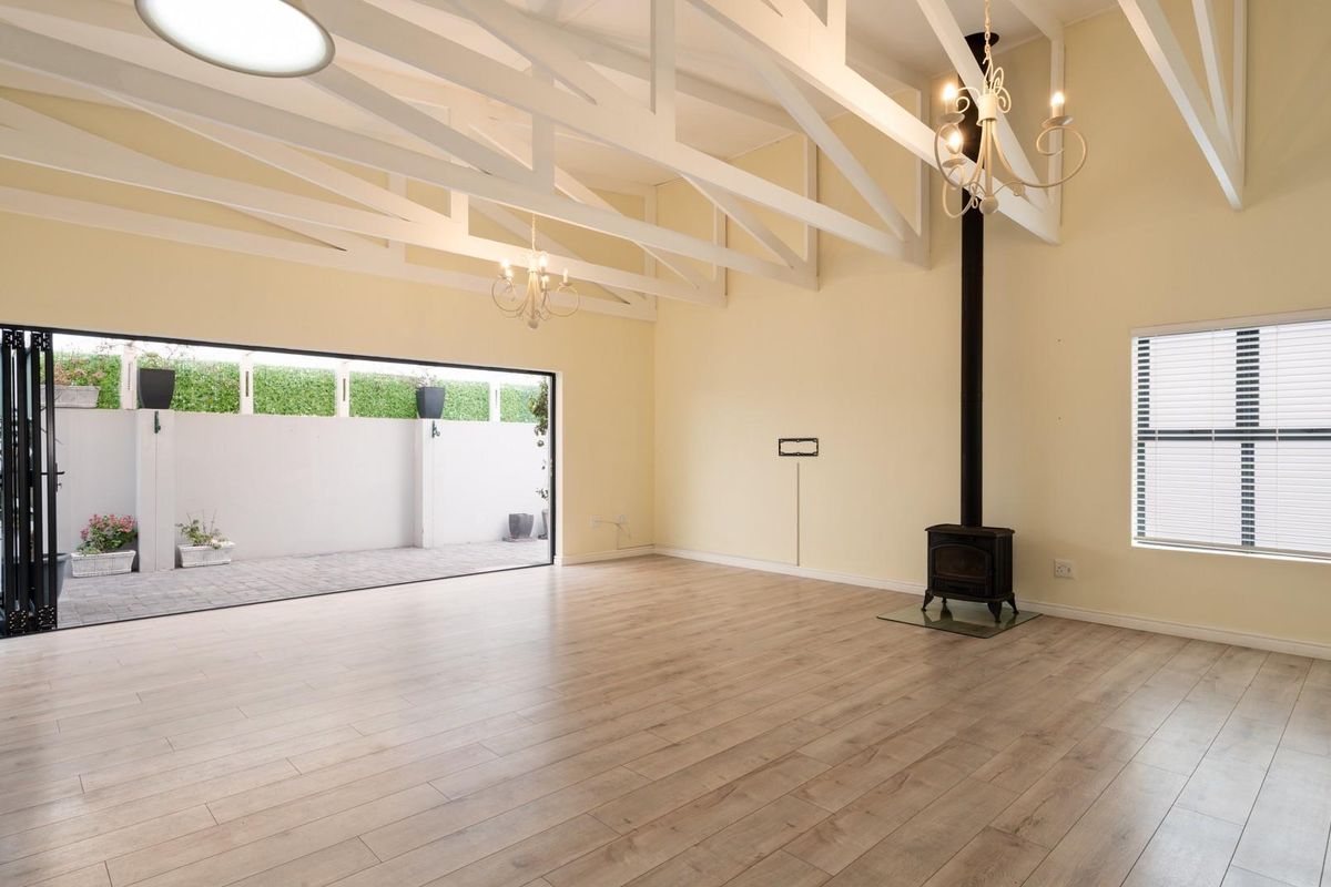 Spacious living area featuring high vaulted ceilings with exposed trusses, a wood-burning fireplace, laminate flooring, and large bi-fold doors opening to a private patio.