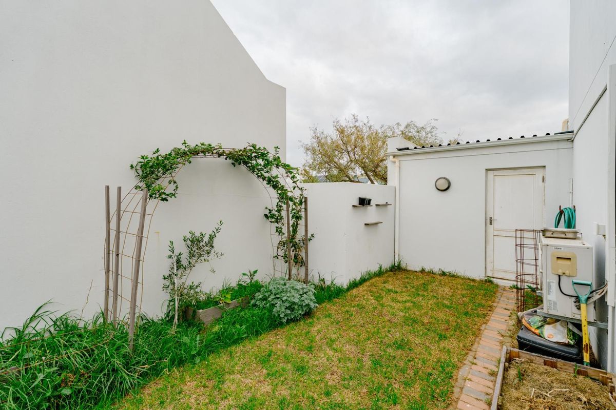 A private rear courtyard area featuring a brick pathway, garden arch, and access to an external door, offering potential for landscaping and outdoor improvement.