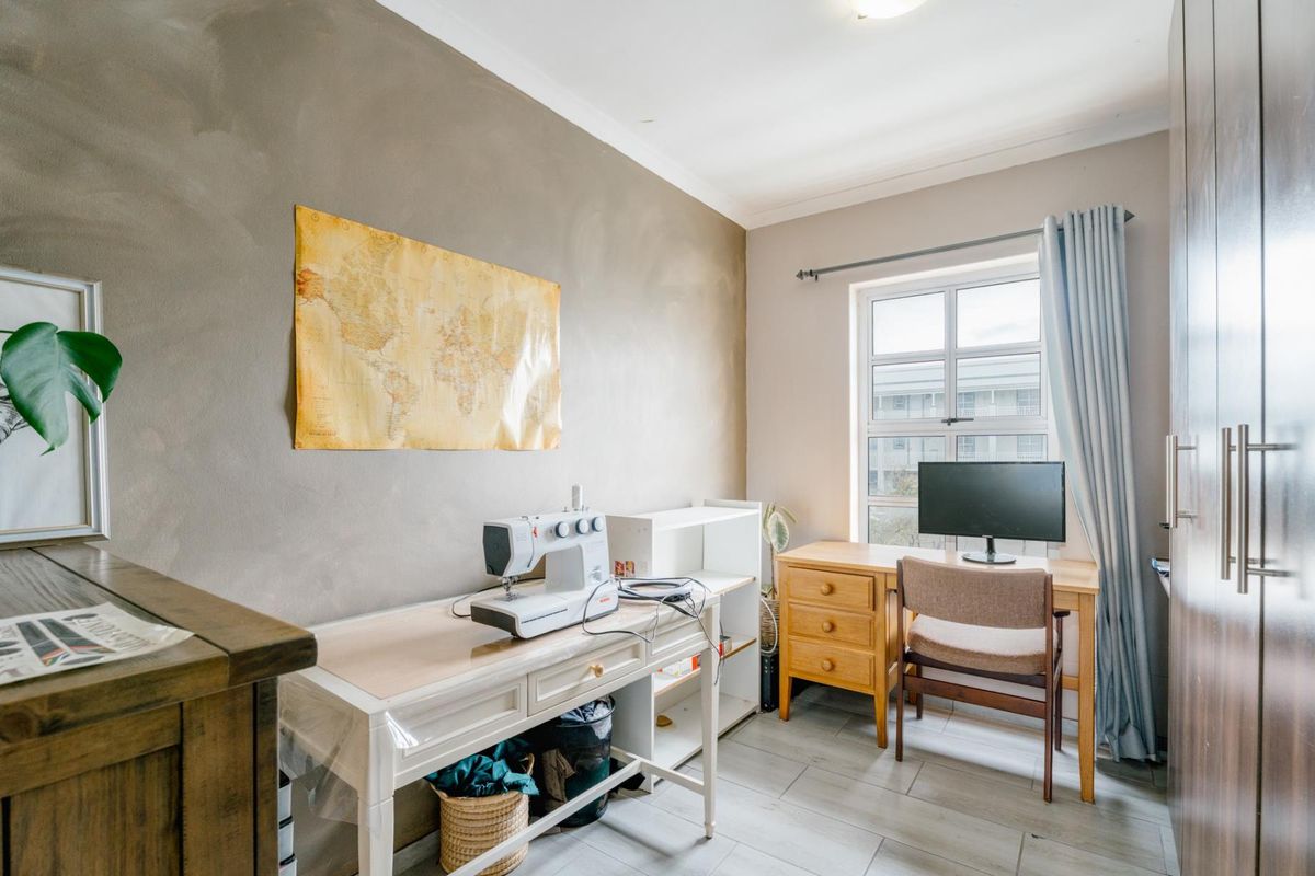 A functional bedroom featuring tiled flooring, built-in cupboards, and a window providing natural light, suitable for use as a bedroom or home office.