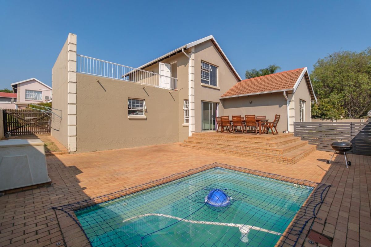 Rear exterior view featuring a paved patio area, a swimming pool with safety net, and a raised terrace leading to the main house structure.