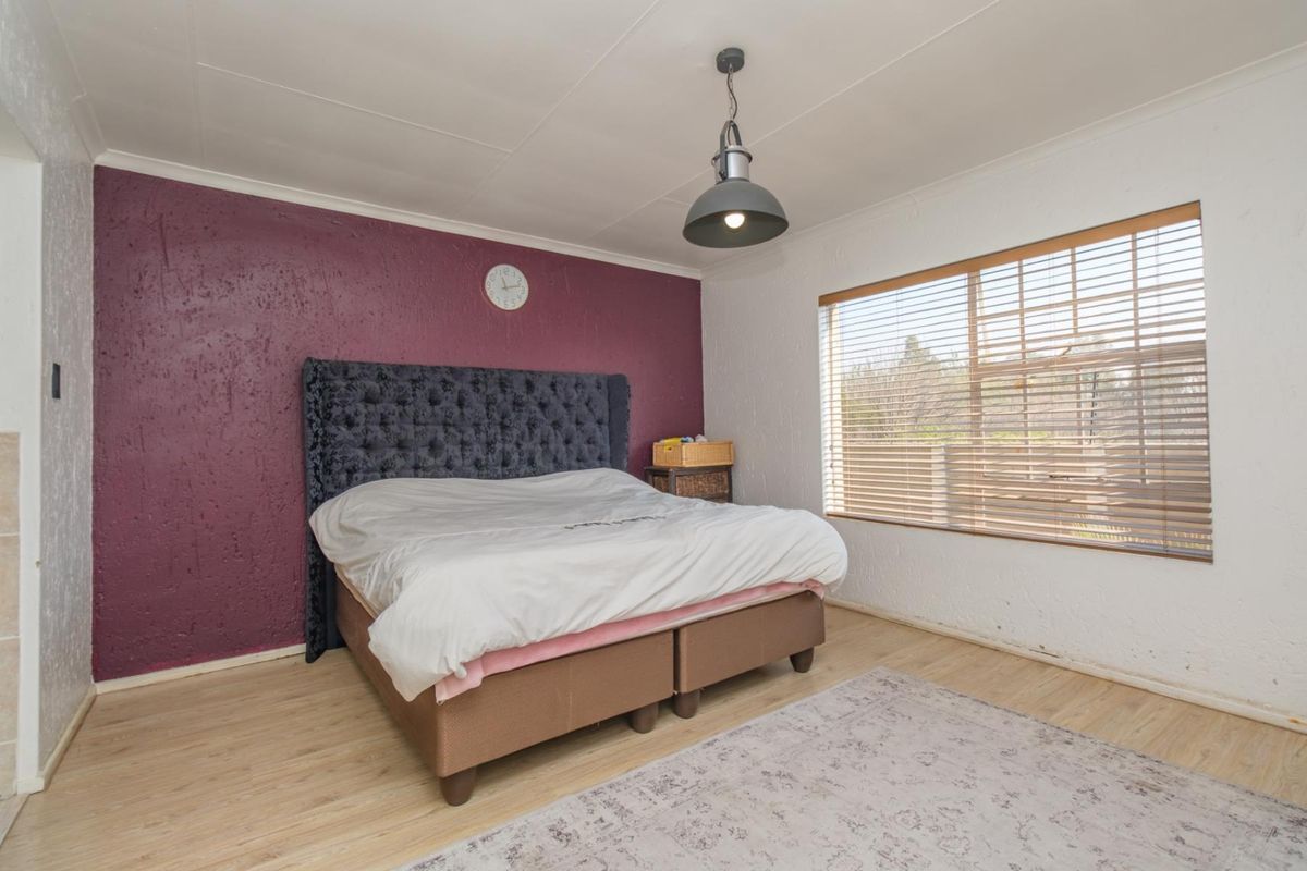 A bedroom featuring laminate flooring, a textured accent wall, and venetian blinds, offering a functional space with potential for cosmetic updates.