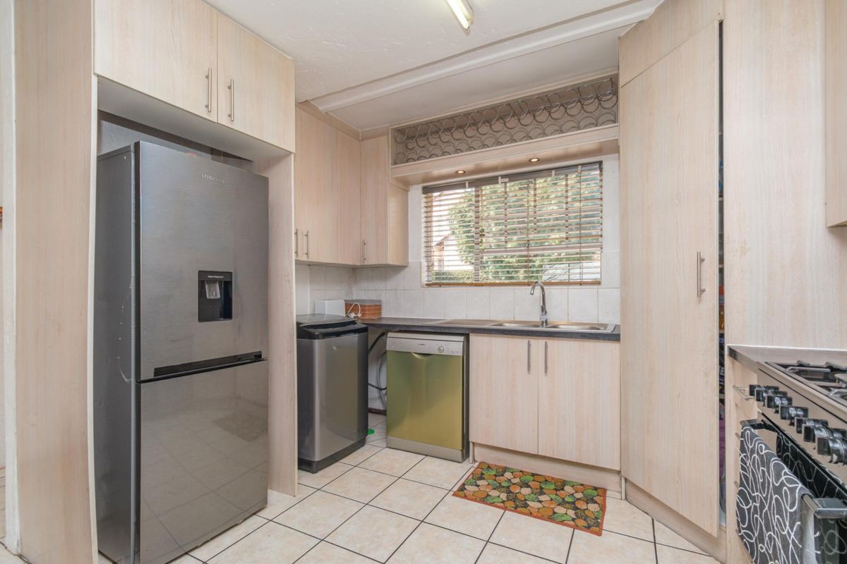 A functional kitchen featuring light wood-finish cabinetry, tiled flooring, a stainless steel sink, and integrated storage solutions with a dedicated wine rack.