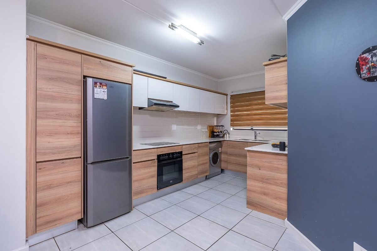 Modern kitchen featuring wood-grain cabinetry, white upper cabinets, integrated appliances, tiled flooring, and a functional layout with ample counter space.