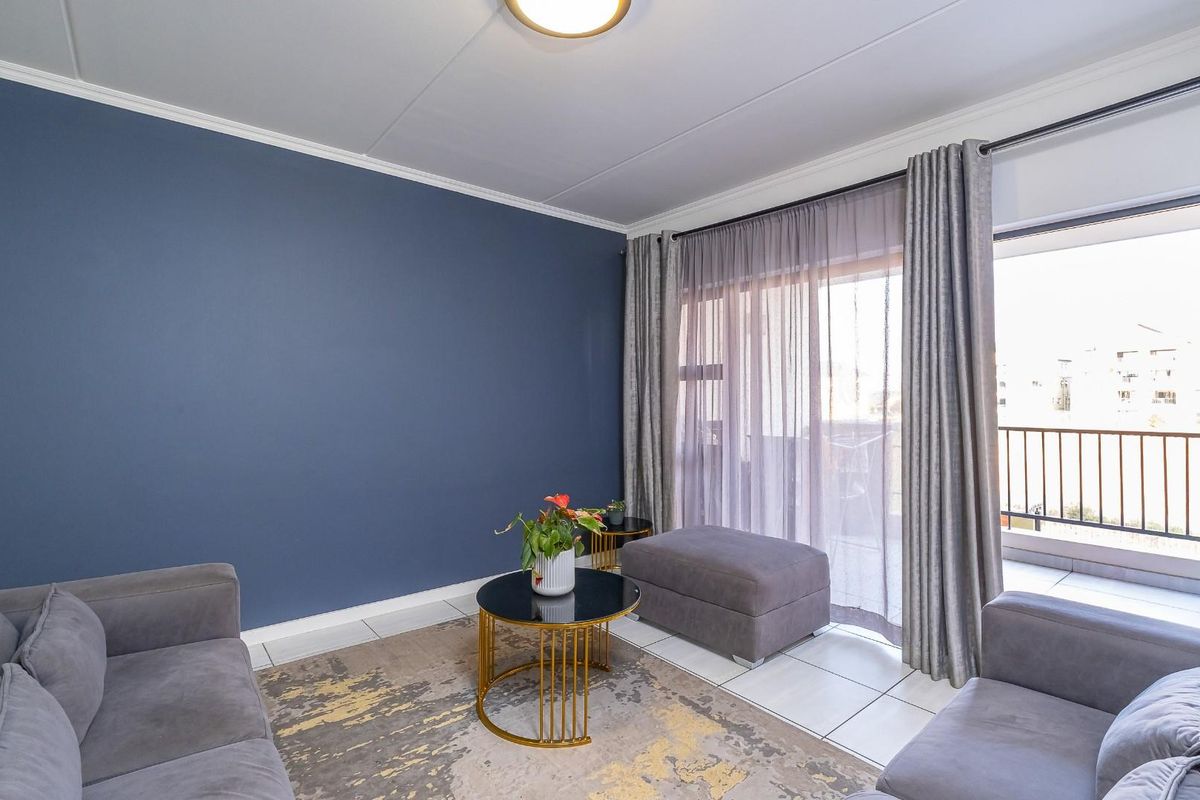 A well-maintained living room featuring tiled flooring, a bold blue accent wall, and a sliding glass door providing direct access to a private balcony.
