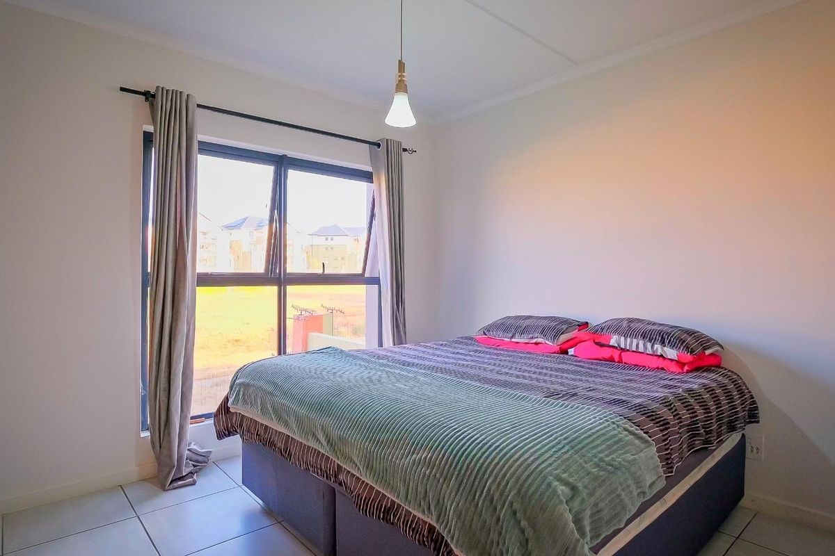 A bright bedroom featuring neutral tiled flooring, a large aluminium-framed window, and a simple pendant light fixture.