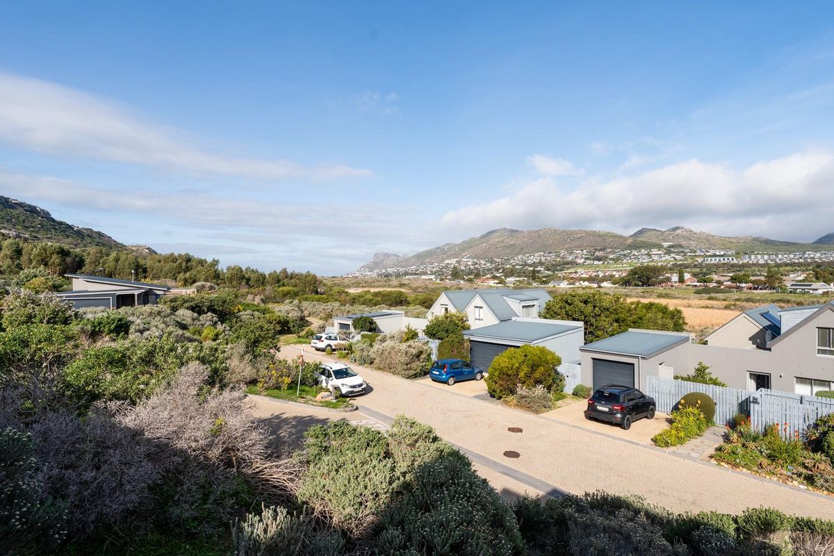 An elevated aerial view of a residential estate featuring paved driveways, modern homes with pitched metal roofs, and surrounding natural landscape.