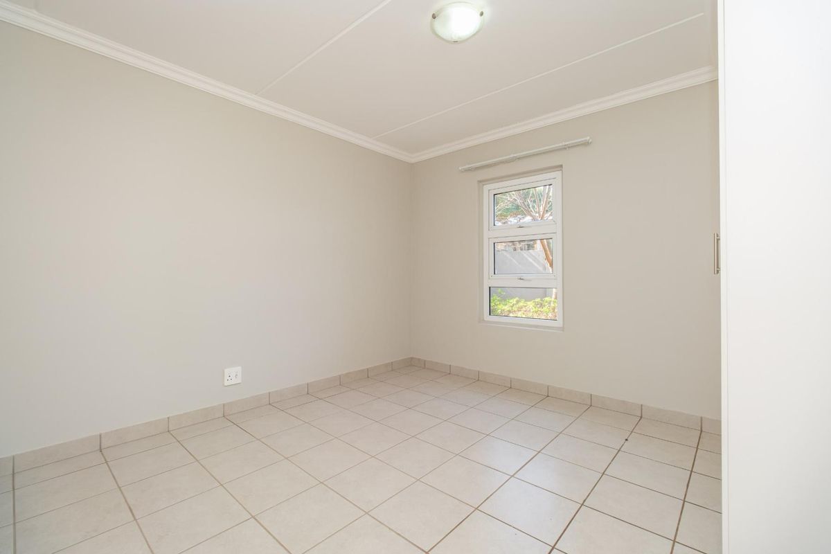 A clean, empty bedroom featuring neutral tiled flooring, built-in cupboard storage, and a window providing natural light.