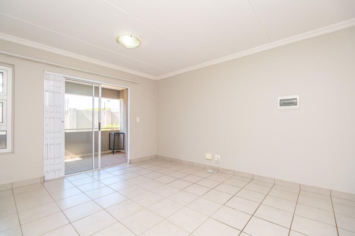 A bright, empty living room featuring neutral tiled flooring and a sliding glass door providing access to an outdoor balcony area.