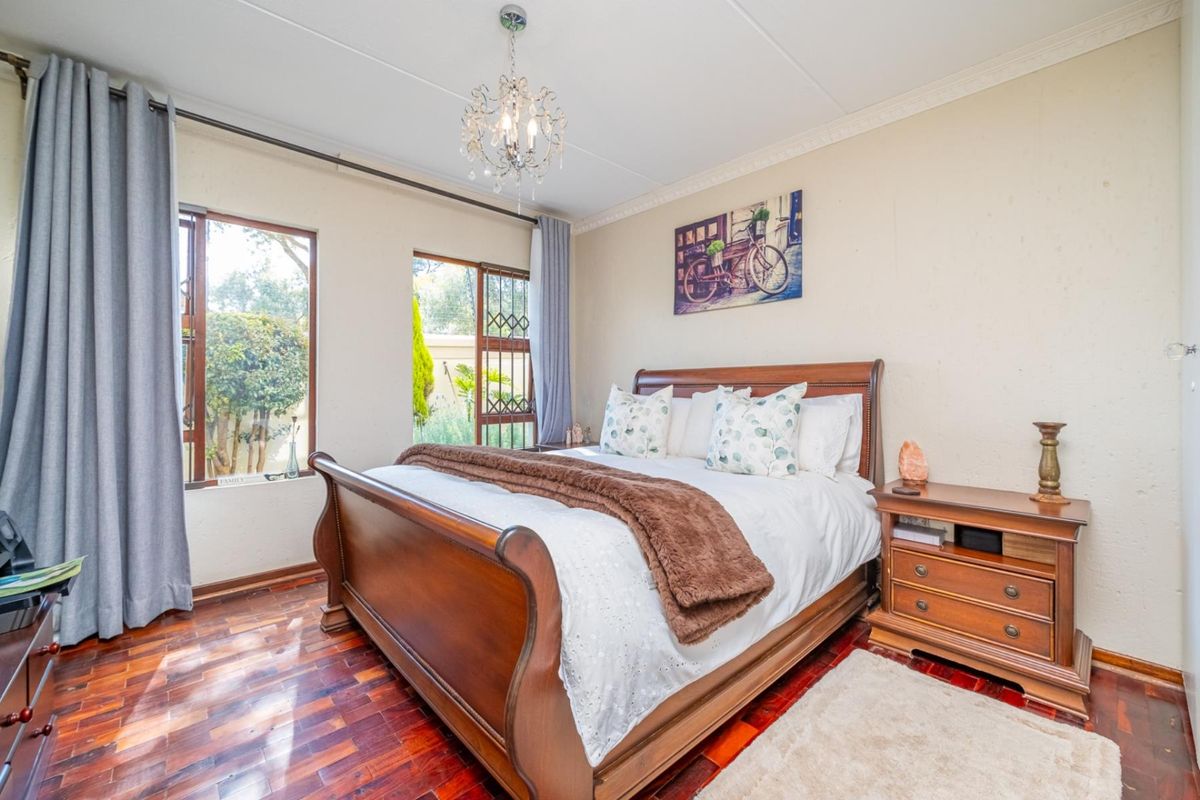 A well-maintained bedroom featuring warm parquet flooring, decorative cornice detailing, and large windows with security gates overlooking the garden.